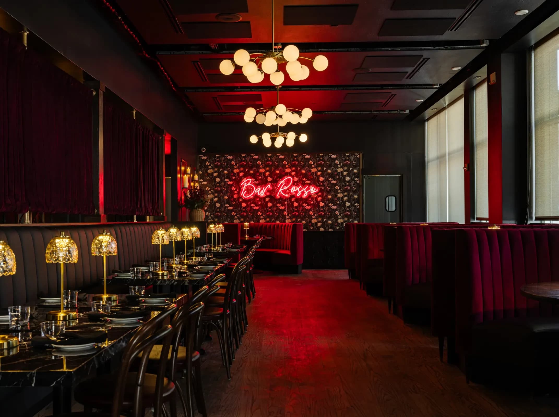 The dining room at Bar Rosso under its neon sign, with red velvet booths and brass table lamps
