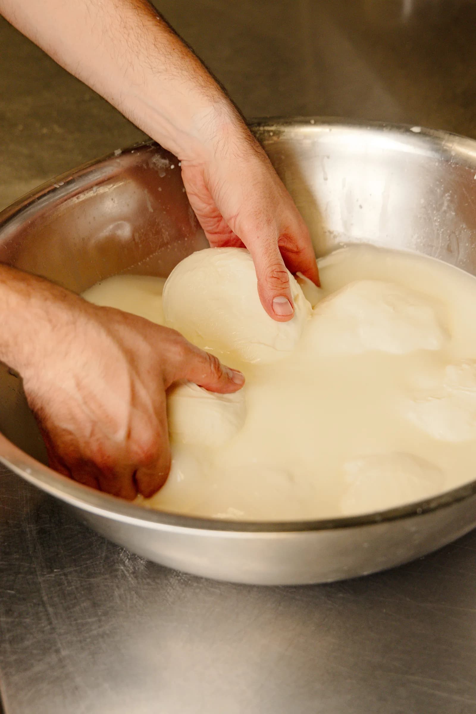 Mozzarella being pulled by hand in a steel bowl