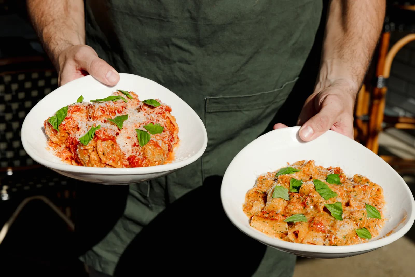 Two plates of pasta carried out to the table by a cook in an apron